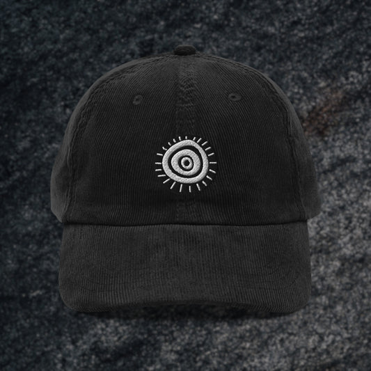 A black corduroy cap with an embroidered circular staring eye