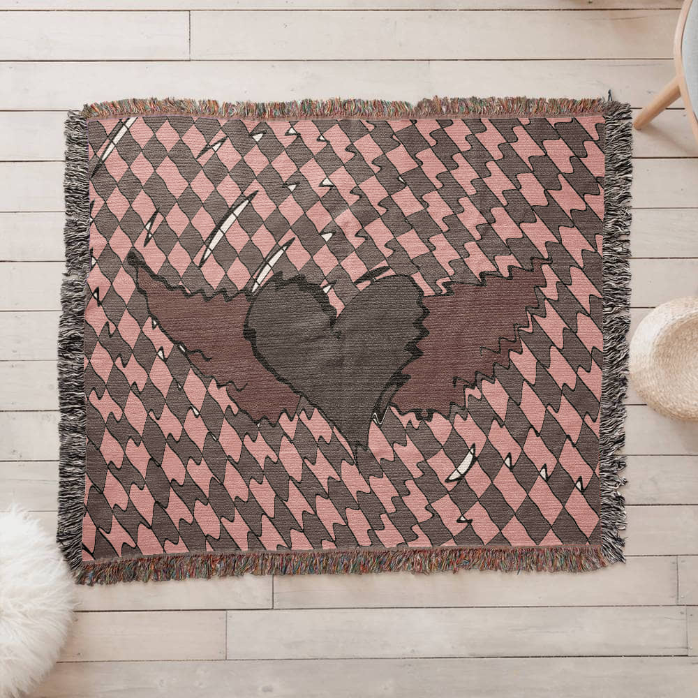 a woven blanket with a deep red heart with wings on a distorted checkered pattern on a wooden floor