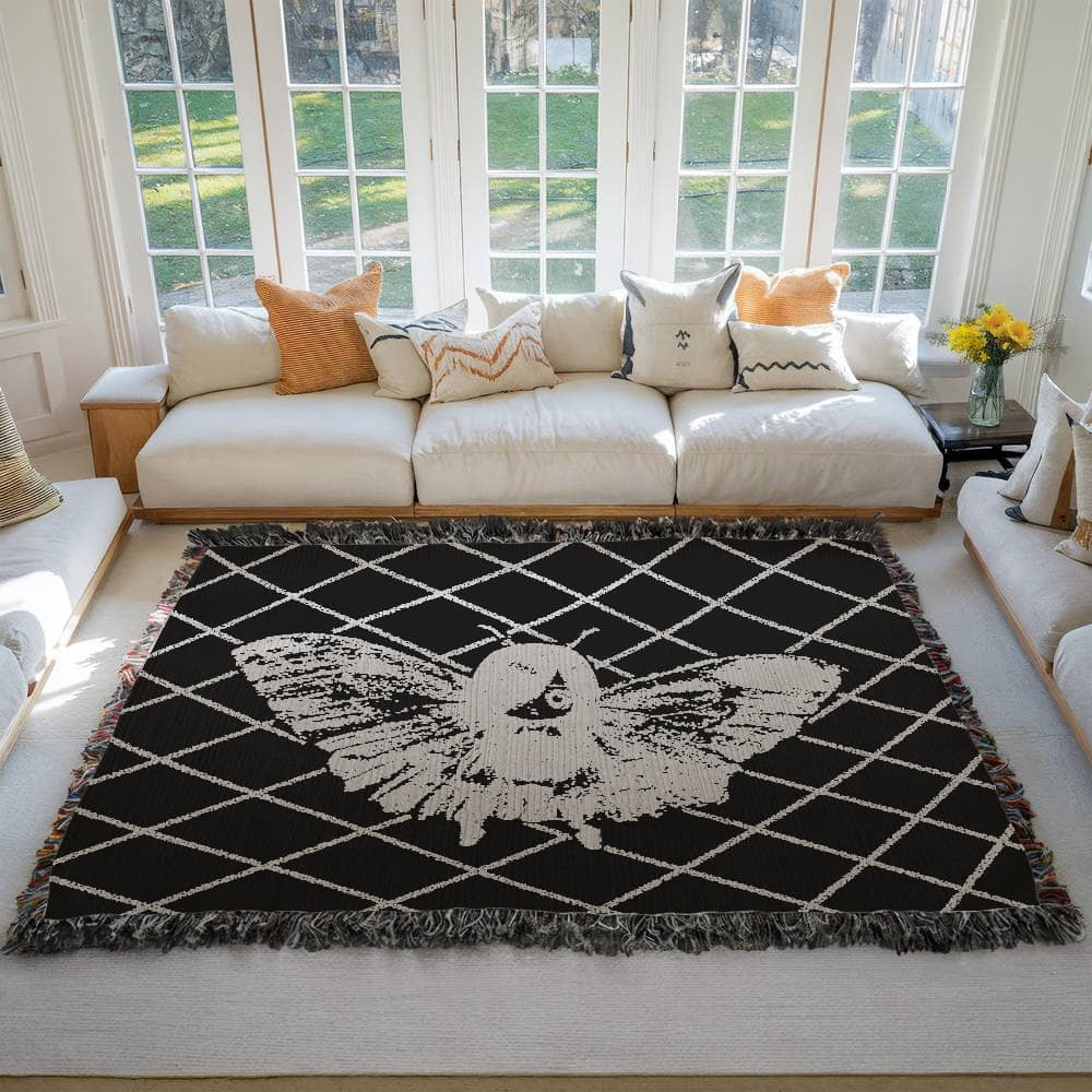 a large woven blanket featuring a moth girl, wings spread on a background of a lattice grid on a living room floor