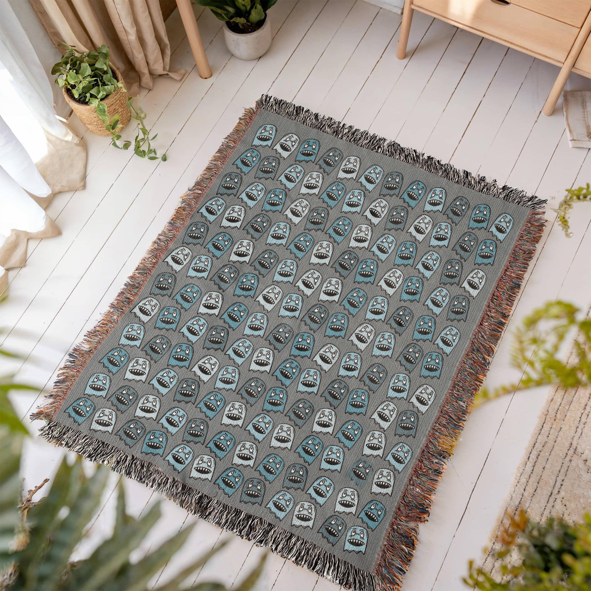 A woven blanket with grinning blue shade goblins on a grey background