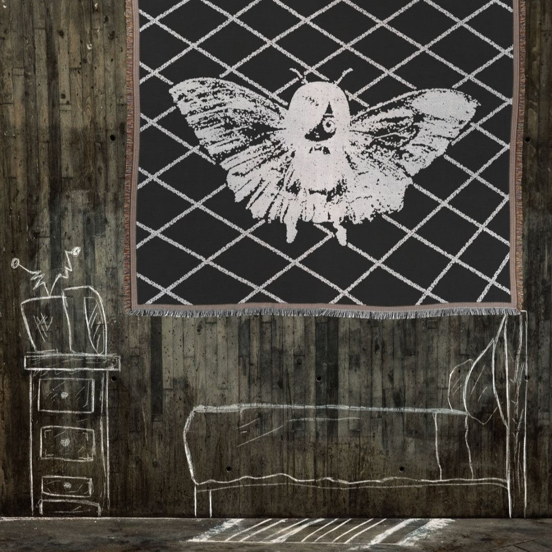a woven blanket featuring a moth girl on a black background in a dark wood panel room