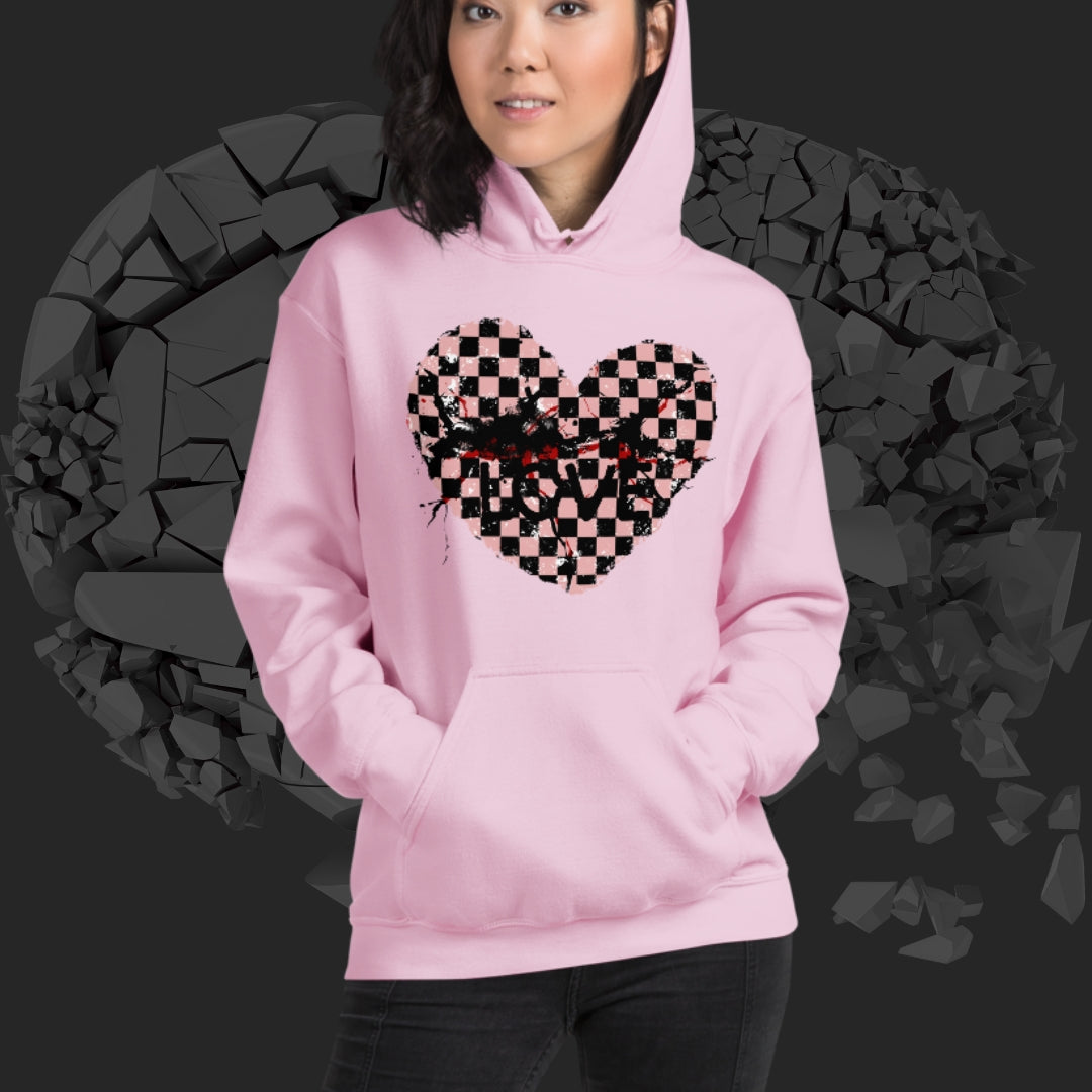 Person wearing a pink hoodie with a pink checkered and distressed heart design against a dark background