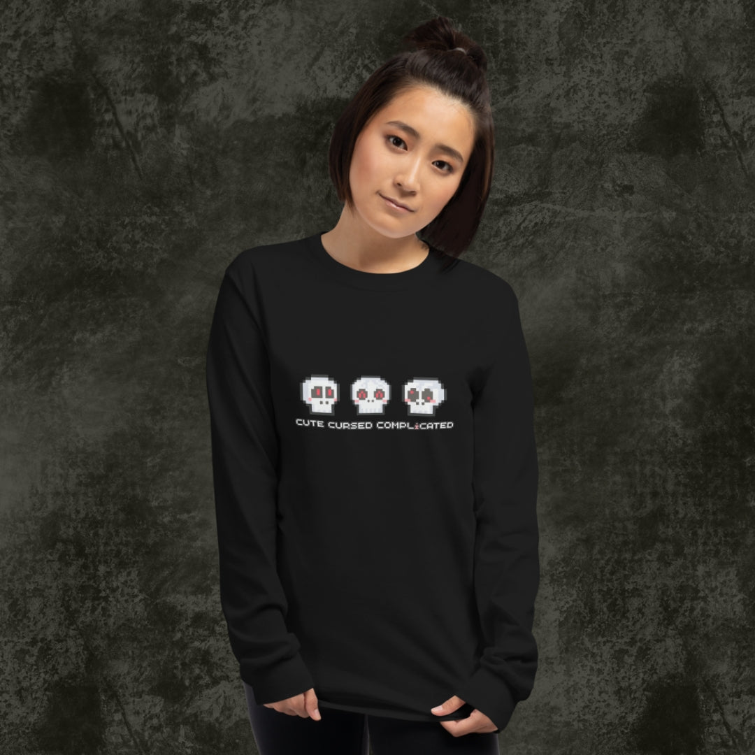 Person wearing a long sleeve tee with pixel art cute skulls and text "cute cursed complicated"