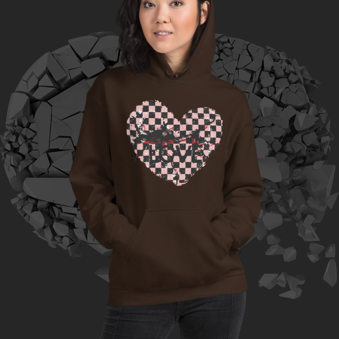 Person wearing a brown  hoodie with a pink checkered and distressed heart design against a dark background