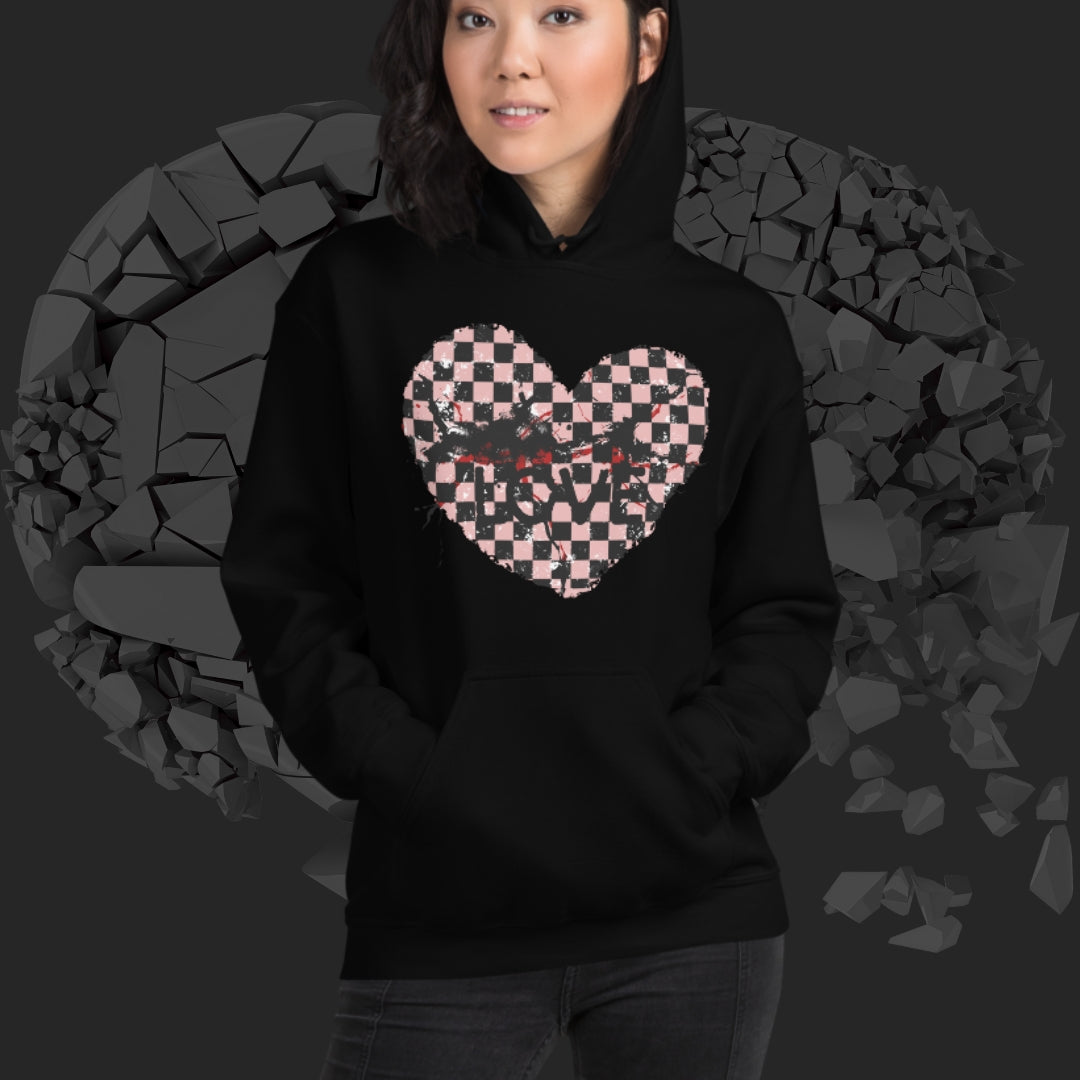 Person wearing a black hoodie with a pink checkered and distressed heart design against a dark background