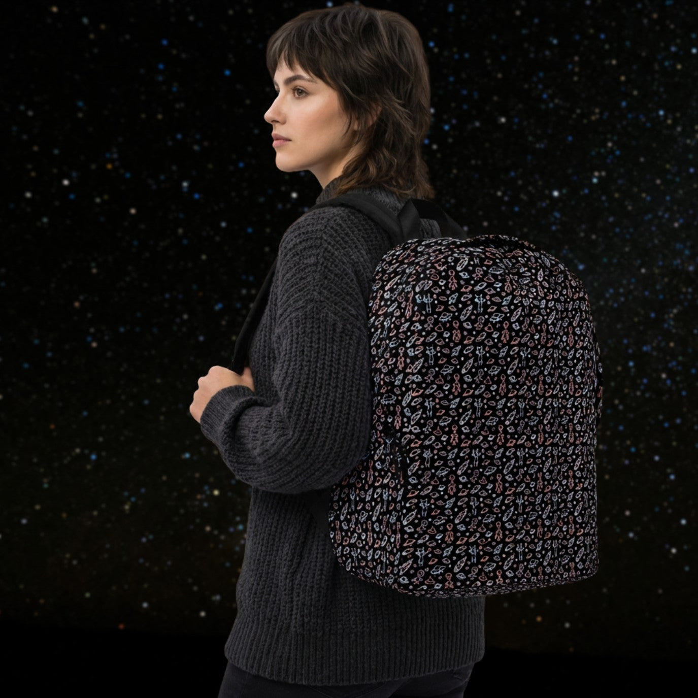 Woman wearing a backpack with a hand drawn space pattern featuring scattered confused aliens, planets, comets, and UFOs in pastel on black. 