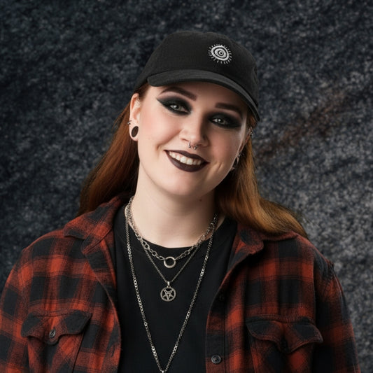 An alt style person wearing a black corduroy cap with an embroidered circular staring eye a red plaid jacket, and dark makeup.