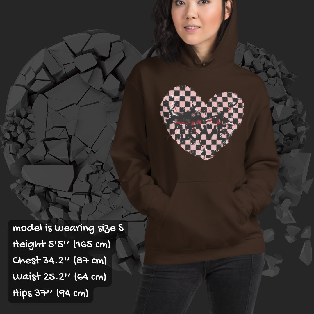 Person wearing a brown  hoodie with a pink checkered and distressed heart design against a dark background