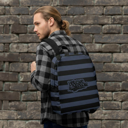 Man with a flannel and ponytail is carrying a backpack with blue and black grunge style dark stripes and text "here we are now" in graffiti tag style