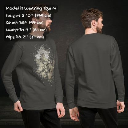 Person wearing a cotton heritage M2480 sweatshirt with a subtle skull graphic surrounded and overlaid with paint splatter in camouflage colors with sizing info