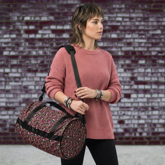 Alt trendy woman in pink sweater carrying a duffel gym bag with a camo, paint splatter, and gritty skulls pattern