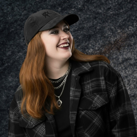 Alt style person with dark plaid flannel and necklaces wearing a vintage corduroy cap with en emo eye embroidery