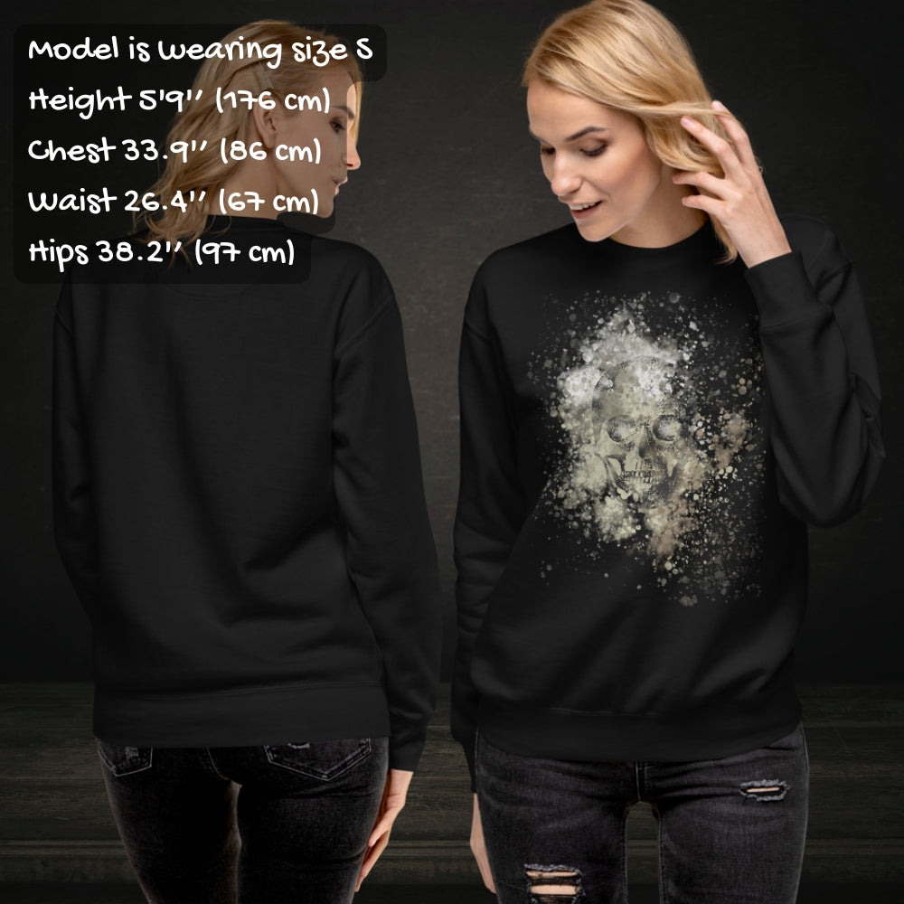 Person wearing a black cotton heritage M2480 sweatshirt with a subtle skull graphic surrounded and overlaid with paint splatter in camouflage colors with sizing info