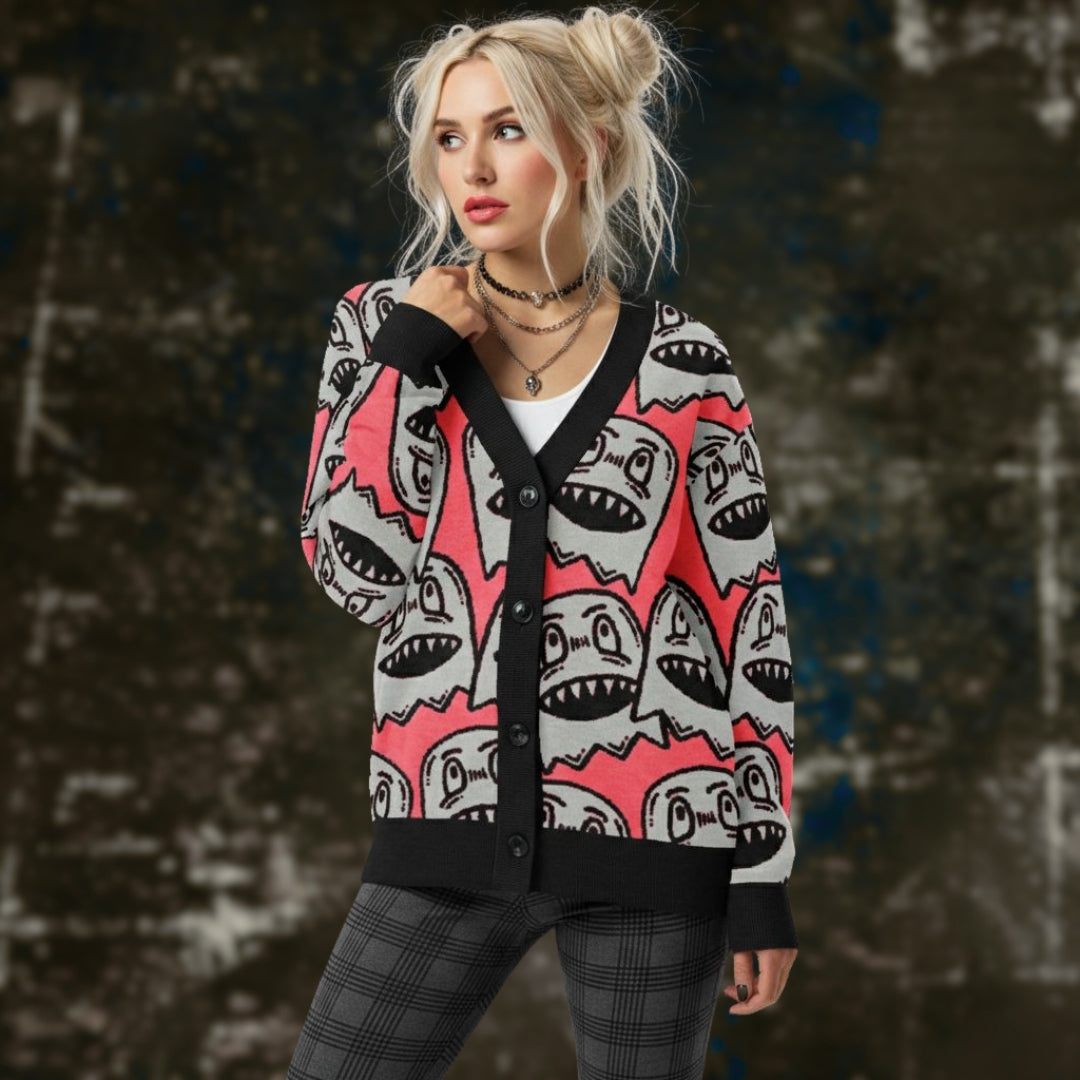 An alt style woman is wearing a hot pink knitted cardigan with large grey grinning goblins and dark plaid leggings.