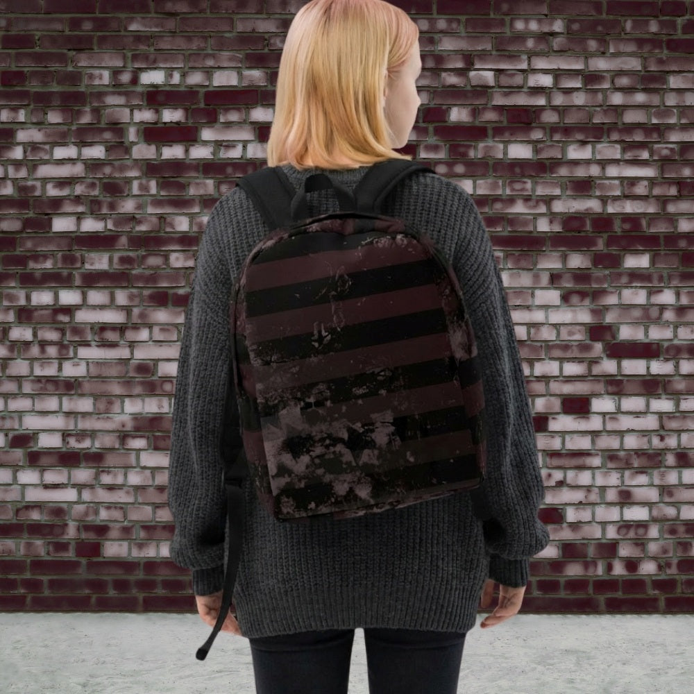 Girl wearing a grunge striped backpack in deep burgundy red and black, with a grungy collage that's visible close-up. 