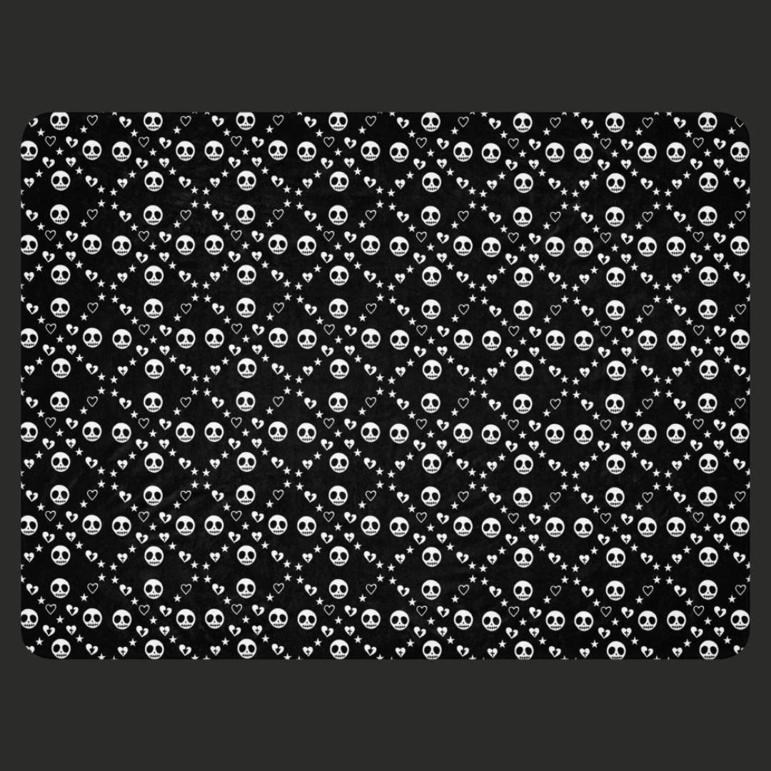 Black sherpa blanket with repeating white skull/ghoul, heart, and star geometric pattern, alt and emo aesthetic throw