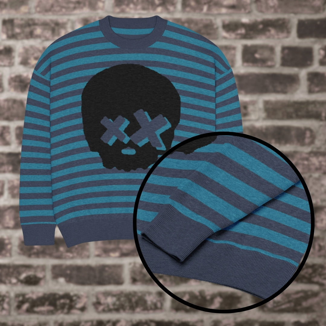 A blue striped knitted sweater with a x-eye skull design against a brick wall
