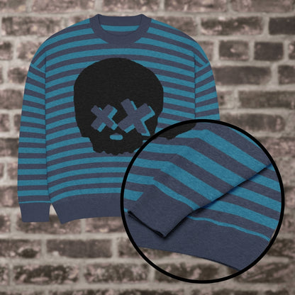 A blue striped knitted sweater with a x-eye skull design against a brick wall