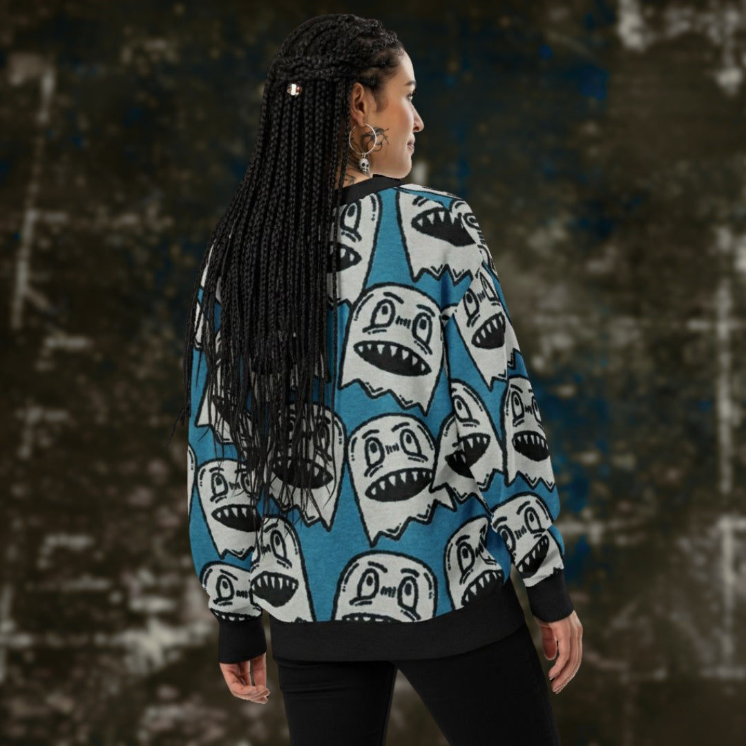 An alt style woman is wearing an electric blue knitted cardigan with large grey grinning goblins and dark leggings.
