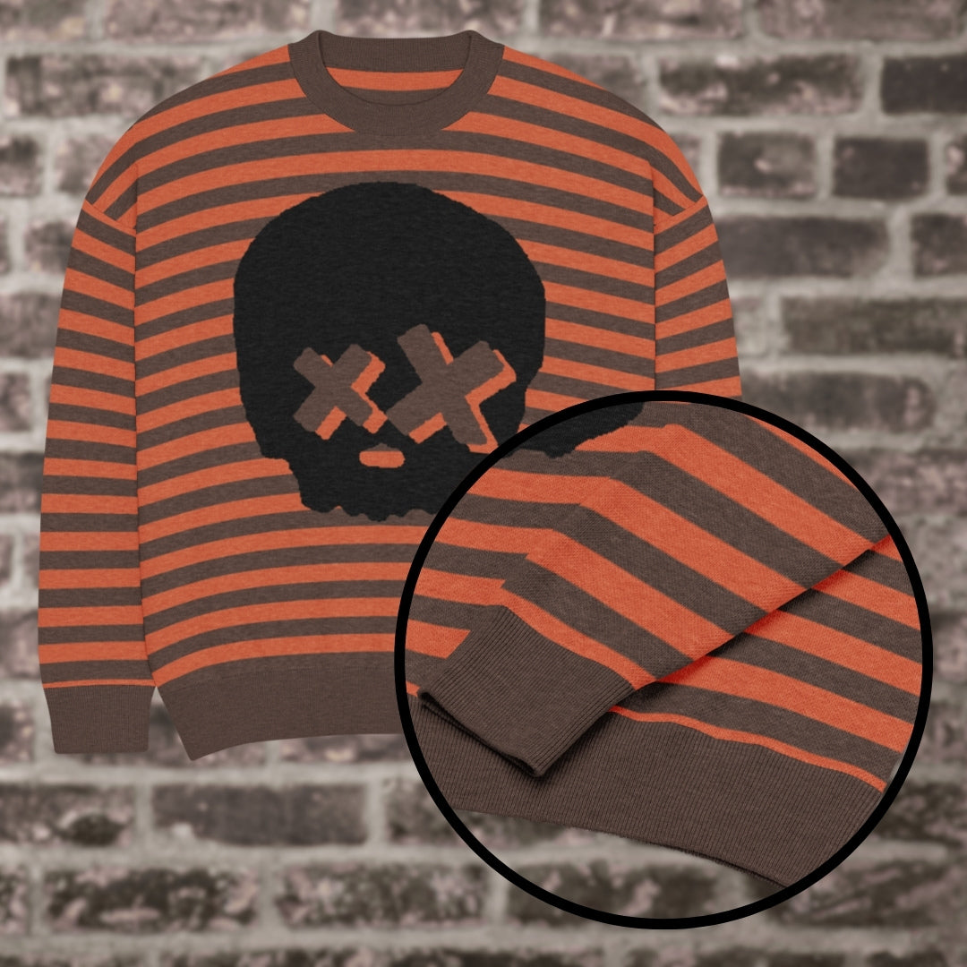 A brown-orange striped knitted sweater with a x-eye skull design against a brick wall