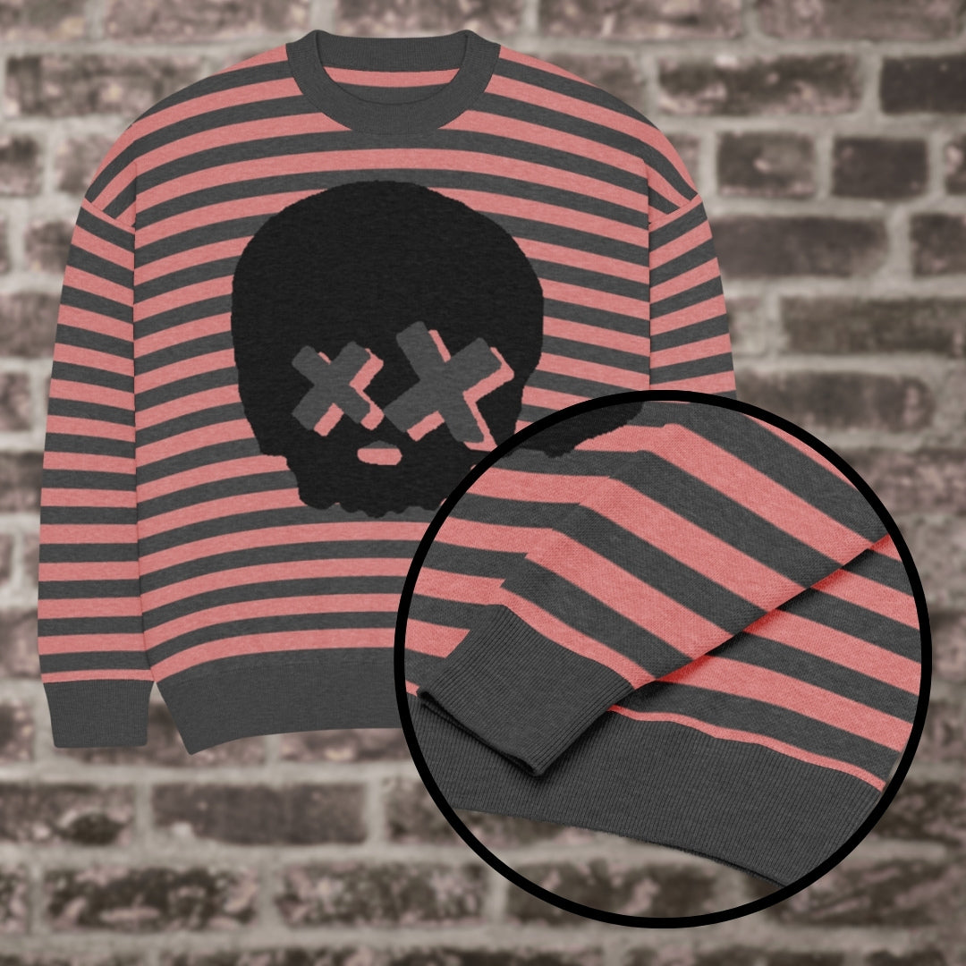 A pink-charcoal striped knitted sweater with a x-eye skull design against a brick wall
