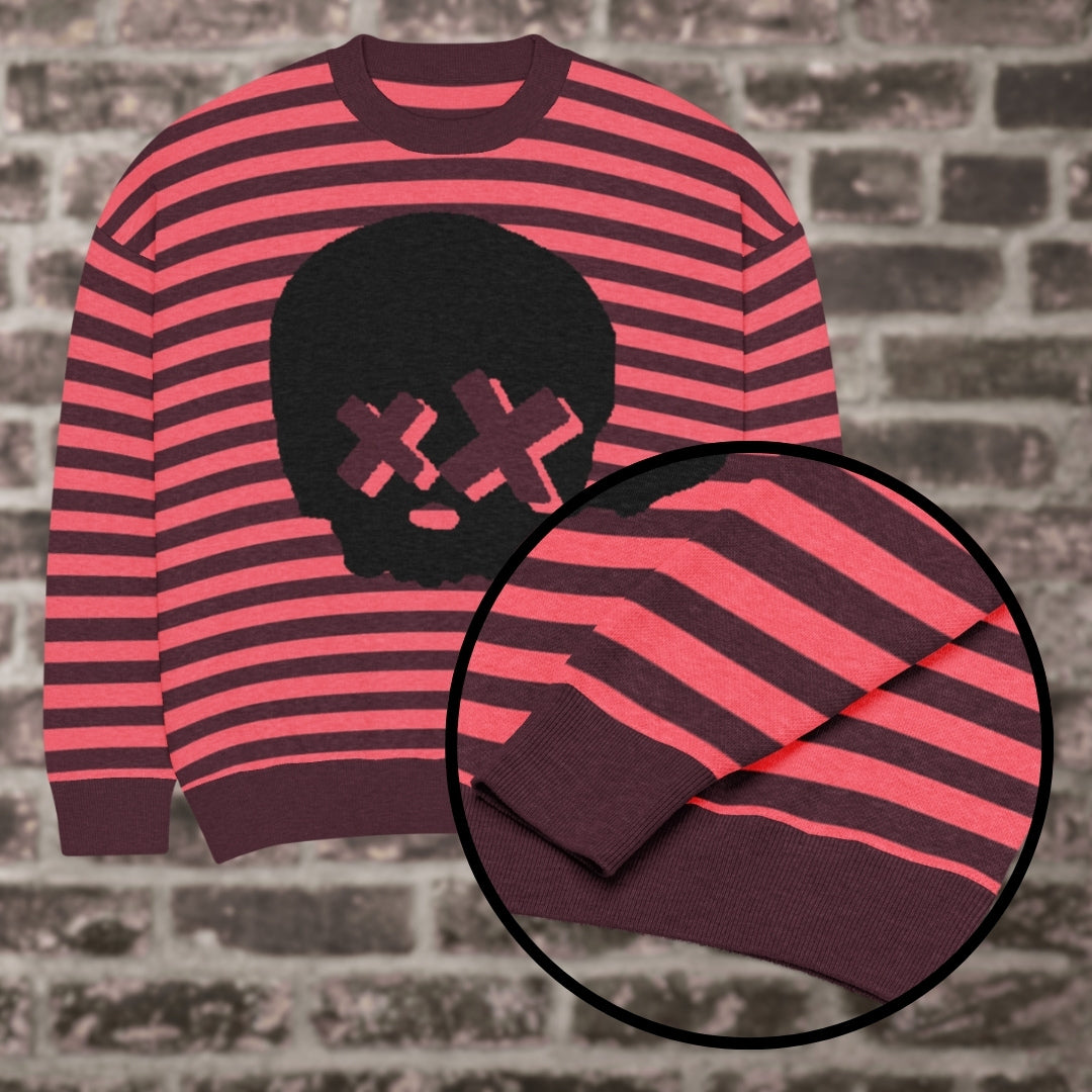A burgundy-hot pink striped knitted sweater with a x-eye skull design against a brick wall