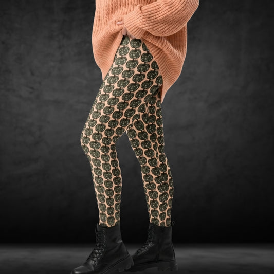Person wearing leggings with camouflage colored pumpkins on peach background, together with a large knit and boots