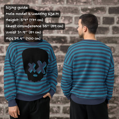 Two people wearing blue striped sweaters with a skull design, standing against a brick wall, with sizing info