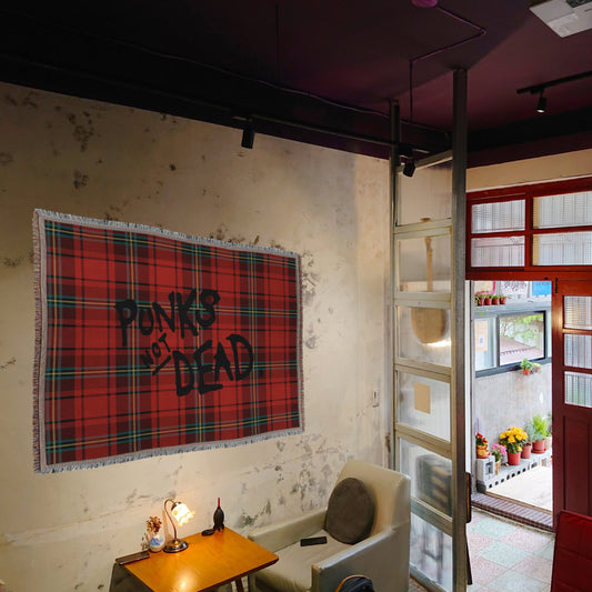 Red plaid woven blanket blanket with 'Punks Not Dead' text on a wall