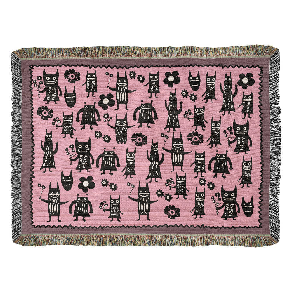 a pink woven blanket featuring grinning goon-goblins and flowers