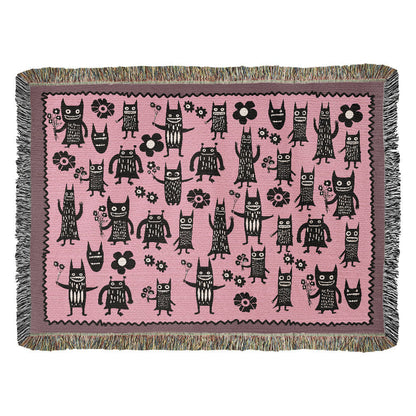 a pink woven blanket featuring grinning goon-goblins and flowers
