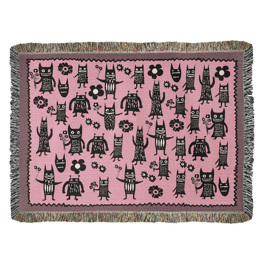 a pink woven blanket featuring grinning goon-goblins and flowers
