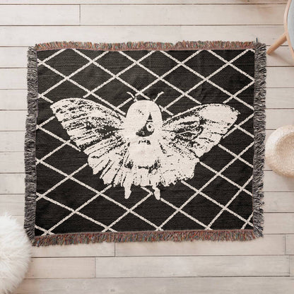 a woven blanket featuring a moth girl, wings spread on a background of a lattice grid on a wooden floor