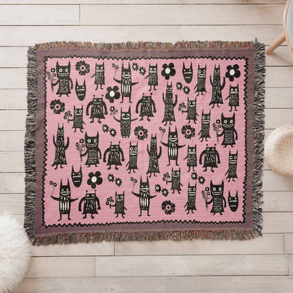 a pink woven blanket featuring grinning goon-goblins and flowers on a floor