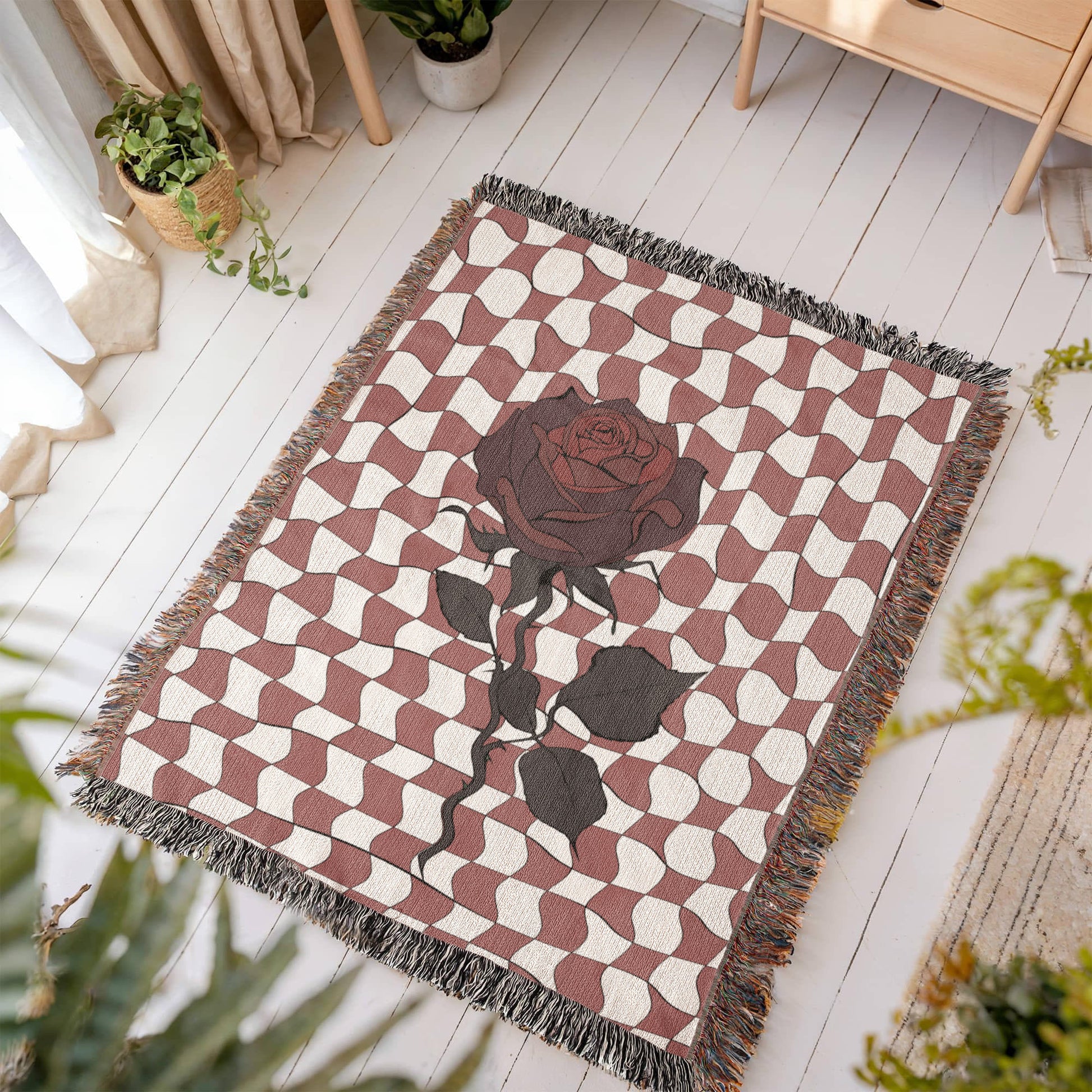 a woven blanket featuring distorted checkerboard patterns and a deep red soulful rose on a wooden floor