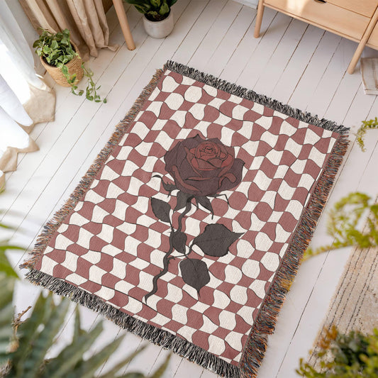 a woven blanket featuring distorted checkerboard patterns and a deep red soulful rose on a wooden floor