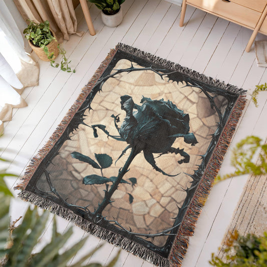 a woven blanket with a black wilted rose and shattered beige background, surrounded by a frame of thorns