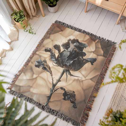 a woven blanket with a black wilted rose and shattered beige background
