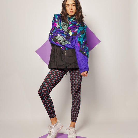 Woman wearing a colorful jacket and diamond patterned leggings on a plain background