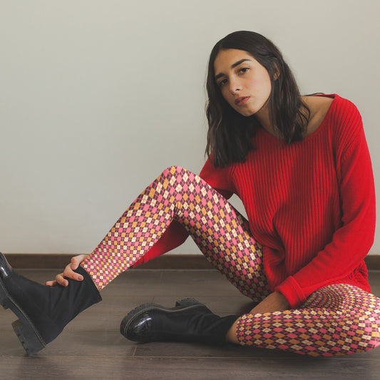 Woman sitting on the floor wearing a red sweater and burgundy diamond patterned leggings.