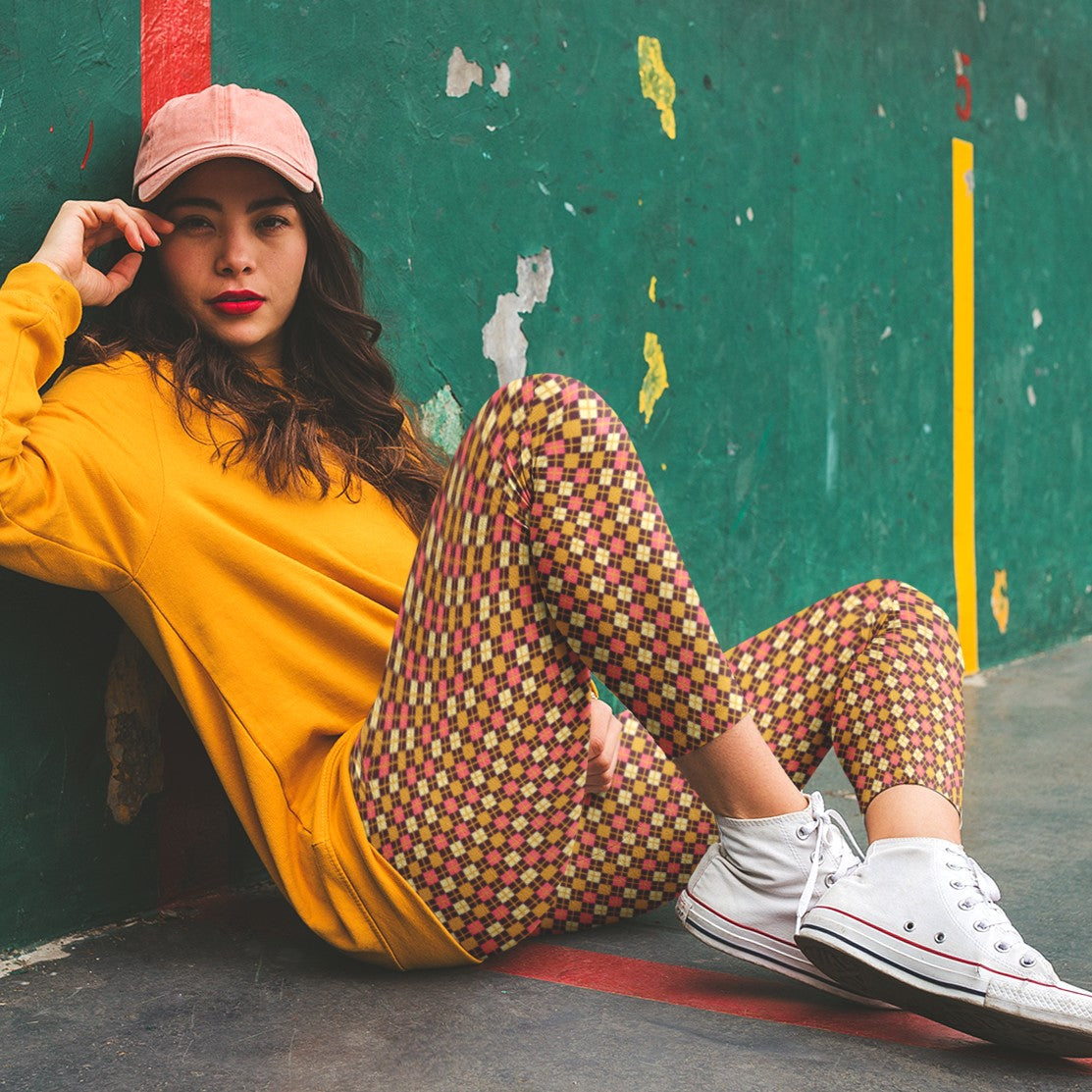 Woman sitting against a colorful wall wearing a yellow sweatshirt, burgundy diamond patterned leggings.