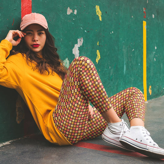 Woman sitting against a colorful wall wearing a yellow sweatshirt, burgundy diamond patterned leggings.