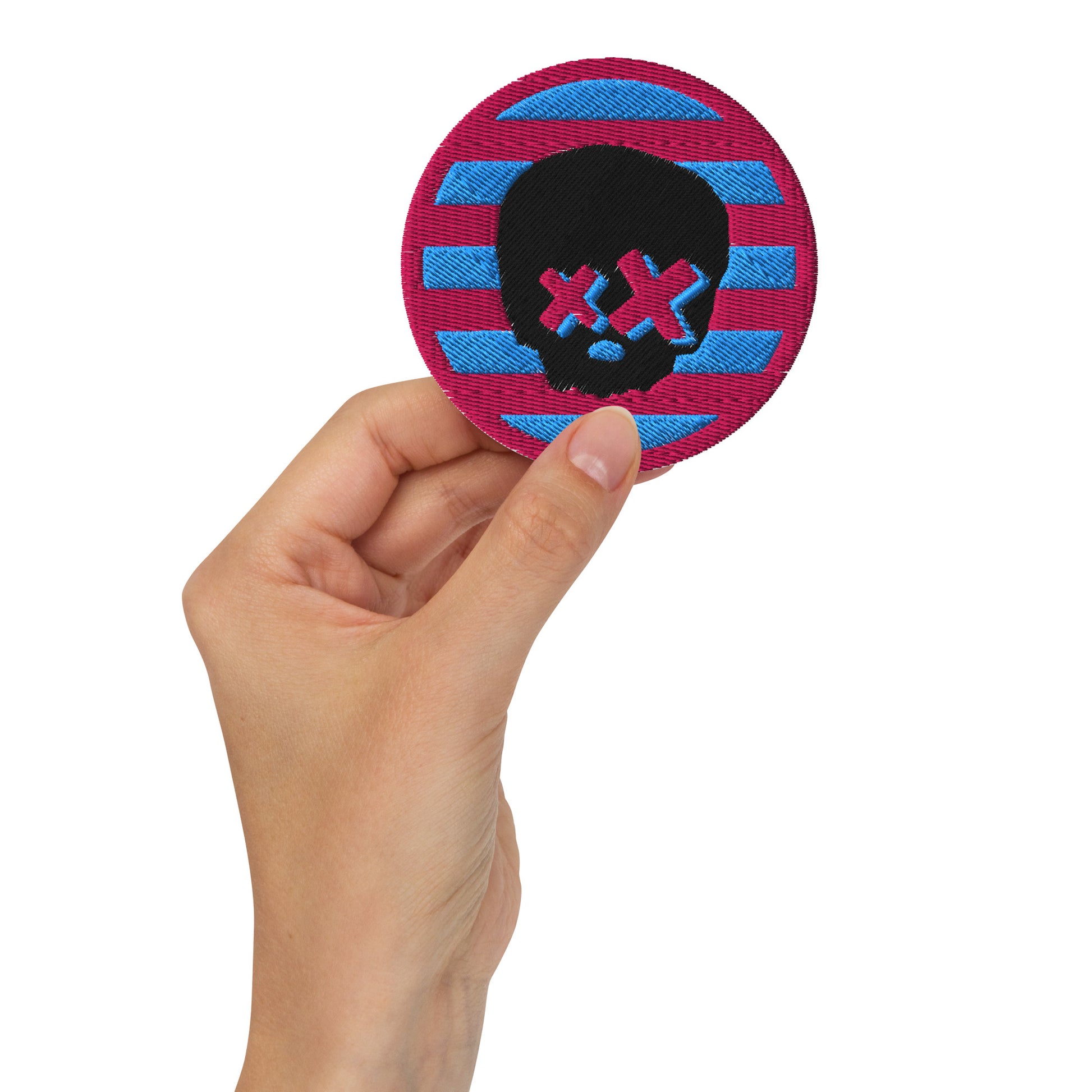 A grunge/emo/scene style embroidered patch with an X-eyed skull on pink and blue stripes
