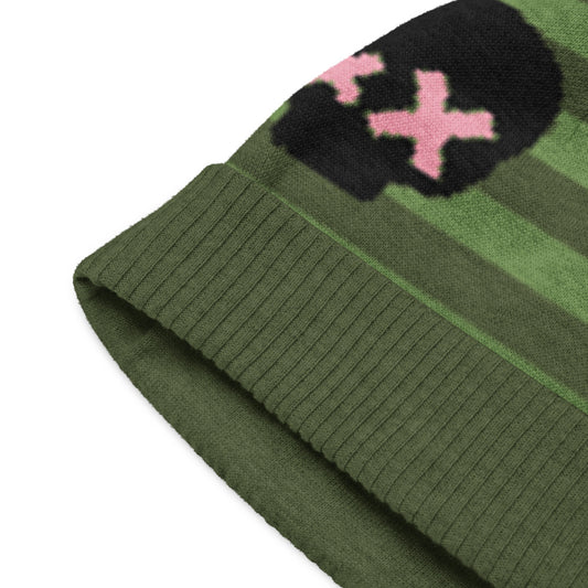 detail of a green striped beanie with a black skull and pink x-eyes 