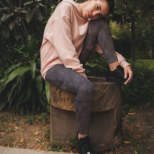 Person sitting on a log in a forested area wearing a pink hoodie and mosaic pattern leggings.