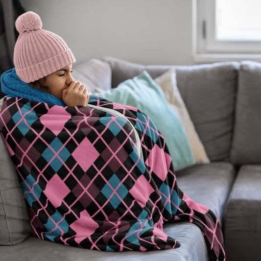 Person wrapped in a colorful argyle pattern blanket on a couch, wearing a pink knit hat.