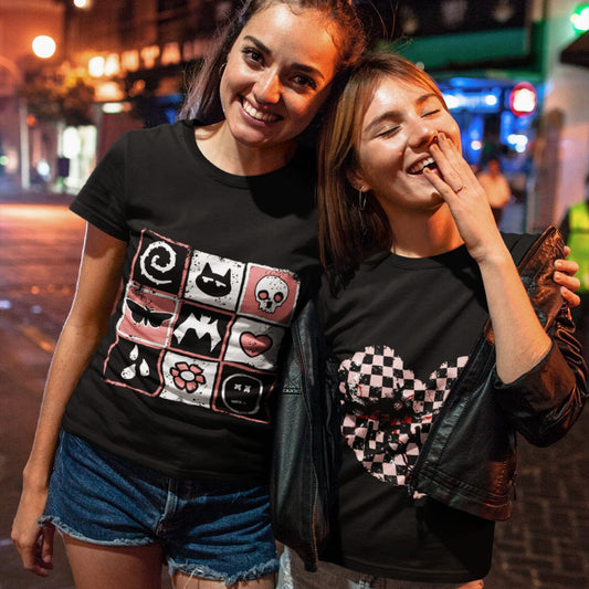 Two women wearing black alt t-shirts with graphic designs, one is a distressed grid of emo symbols, spelling emo diagonally