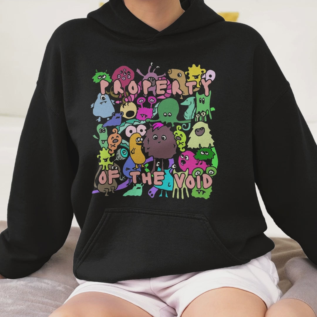 a woman wearing a black hoodie with front print a colorful horde of goblins and text "property of the void" and on the back, the goblins' back sides