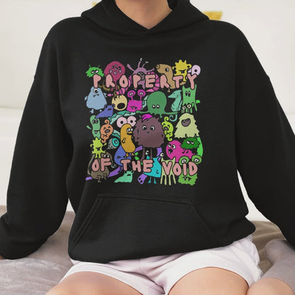 a woman wearing a black hoodie with front print a colorful horde of goblins and text "property of the void" and on the back, the goblins' back sides