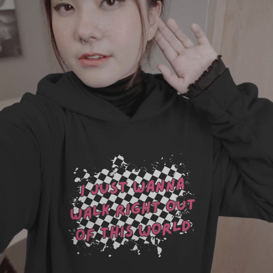 woman wearing a black hoodie with rugged checkers and pink text "i just wanna walk right out of this world" in the front and a checkered road winding away, with text "goodby" on the back